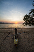 Outrigger boat on an Areia Branca beach at sunset, Dili, East Timor