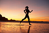 Silhouette einer Frau, die bei Sonnenuntergang am Strand läuft