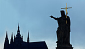 Silhouette of statue and crucifix by church spires, Prague, Bohemia, Czech Republic