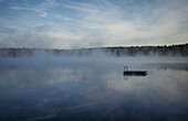 Mist clouds over still lake in remote landscape