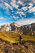 Hiker on rock outcrop overlooks Powerline Pass valley and trail, Chugach State Park, Southcentral Alaska