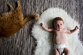 Caucasian baby girl laying on carpet with cat