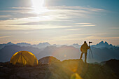 A photographer enjoys the view of the sunrise from his campsite on a rocky mountain ridge.