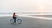 A woman rides a bike on the beach at sunset in Washington State.