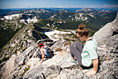 A young couple scramble down granite rock on the summit ridge of Needle Peak, British Columbia, Canada.