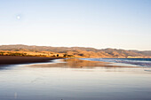 Low tide in northern California reflects the illuminated foothills of Point Reyes on Limantour beach.