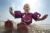 A young girl in floaties splashes in the water at the beach.