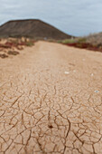 Dry cracked earth in Fuerteventura with a volcanic cone in the background