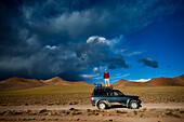 A man stands on the roof of his truck to take a photo of the dramatic sky at sunset near the Salar de Uyuni, Bolivia.