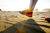 Detail of a woman's running shoe as she walks across a sandy beach near the Pistol River State Scenic Viewpoint, Oregon.