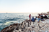 Junge Menschen sitzen am Felsufer der Adriaküste, Rovinj, Istrien, Kroatien