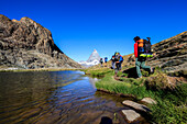 Hikers proceed on the shore of Lake Riffelsee with the Matterhorn in the background, Zermatt, Canton of Valais, Switzerland, Europe