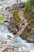Hikers cross the wooden bridge on a creek in the woods, Minor Valley, High Valtellina, Livigno, Lombardy, Italy, Europe