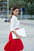 Hispanic businesswoman carrying laptop outdoors