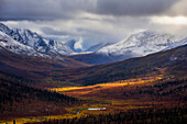 Storm clouds part allowing light to illuminate the landcape in the North Klondike Valley along the Dempster Highway in northern Yukon, Yukon, Canada