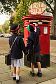 Brother and sister holding hands posting letter, London, England