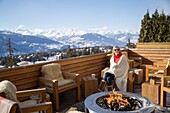 Woman sitting near fire pit on the terrace of a hotel, Crans-Montana, Swiss Alps, Switzerland