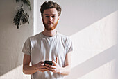 Portrait of confident young man holding mobile phone at home