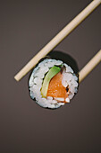 Chopsticks holding sushi against gray background