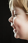 Close-up side view of happy boy against black background
