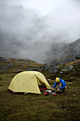 Woman hiker prepares a meal at camp during a backpacking trip to Reed Lakes in the Talkeetna Mountains near Palmer, Alaska August 2011.