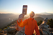 A man uses his smartphone to take a selfie from the summit of a mountain in Washington.