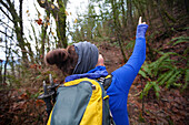 A young active woman points out some wildlife while backpacking through a dense forest.