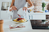 Caucasian woman pouring sauce on pasta in kitchen