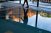Man walking beside pool, reflected on water