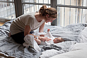 Mother playing with baby girl in bedroom