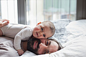 Portrait of loving father with baby girl lying in bed