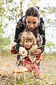 Mother showing mushroom to daughter on field