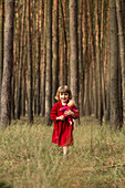 Portrait of cute girl holding doll while standing in forest