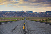 Road leading towards rocky mountains against cloudy sky