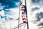 Tattered American flag on pole against cloudy sky