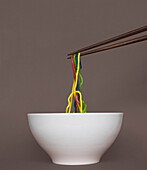 Chopsticks lifting noodles from bowl against gray background