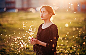 Caucasian woman standing in field with blowing dandelion seeds