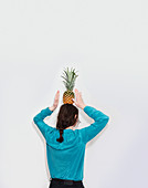 Rear view of woman balancing pineapple while standing against white background