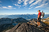A backpacker looks down at Valentine Lake from a rocky ridge near Saxifrage Mountain, Pemberton, British Columbia, Canada.