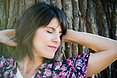Woman resting head on tree trunk, eyes closed