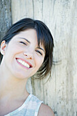 Woman leaning against tree trunk, smilling cheerfully, portrait