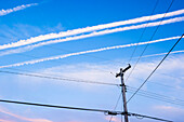 Typical open land phone and power supply lines on wooden posts with condensation trail in the blue sky, Toronto, Canada