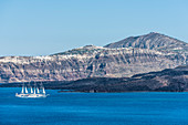 Ein Segelschiff / Kreuzfahrtschiff vor der Kulisse der Insel Santorin mit der Steilküste und dem Dorf Akrotiri im Hintergrund, Santorin, Kykladen, Griechenland
