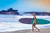 Young woman with surfboard on a beach.