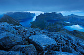 Blick von der Flanke des Hermannsdalstinden im Blau der Dämmerung auf die umliegenden Berge mit eingeschlossenen Seen und den Kjerkfjorden im Hintergrund, Moskenesøy, Lofoten, Norwegen, Skandinavien