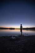 Junger Mann steht an einem See und betrachtet die Sterne, Freilassing, Bayern, Deutschland