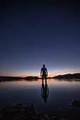 Young man standing in a lake at night, Freilassing, Bavaria, Germany
