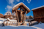 Wooden crucifix in the village of Coi. Winter in Zoldo Alto, Dolomites. In the background the wall of Pelmo mountain.