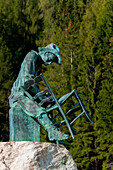 The monument to the chair-maker, Gosaldo, Agordino, Dolomites on the background a forest of firs