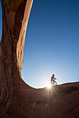 A girl riding a mountain bike along Wilson Arch near Moab, Utah.